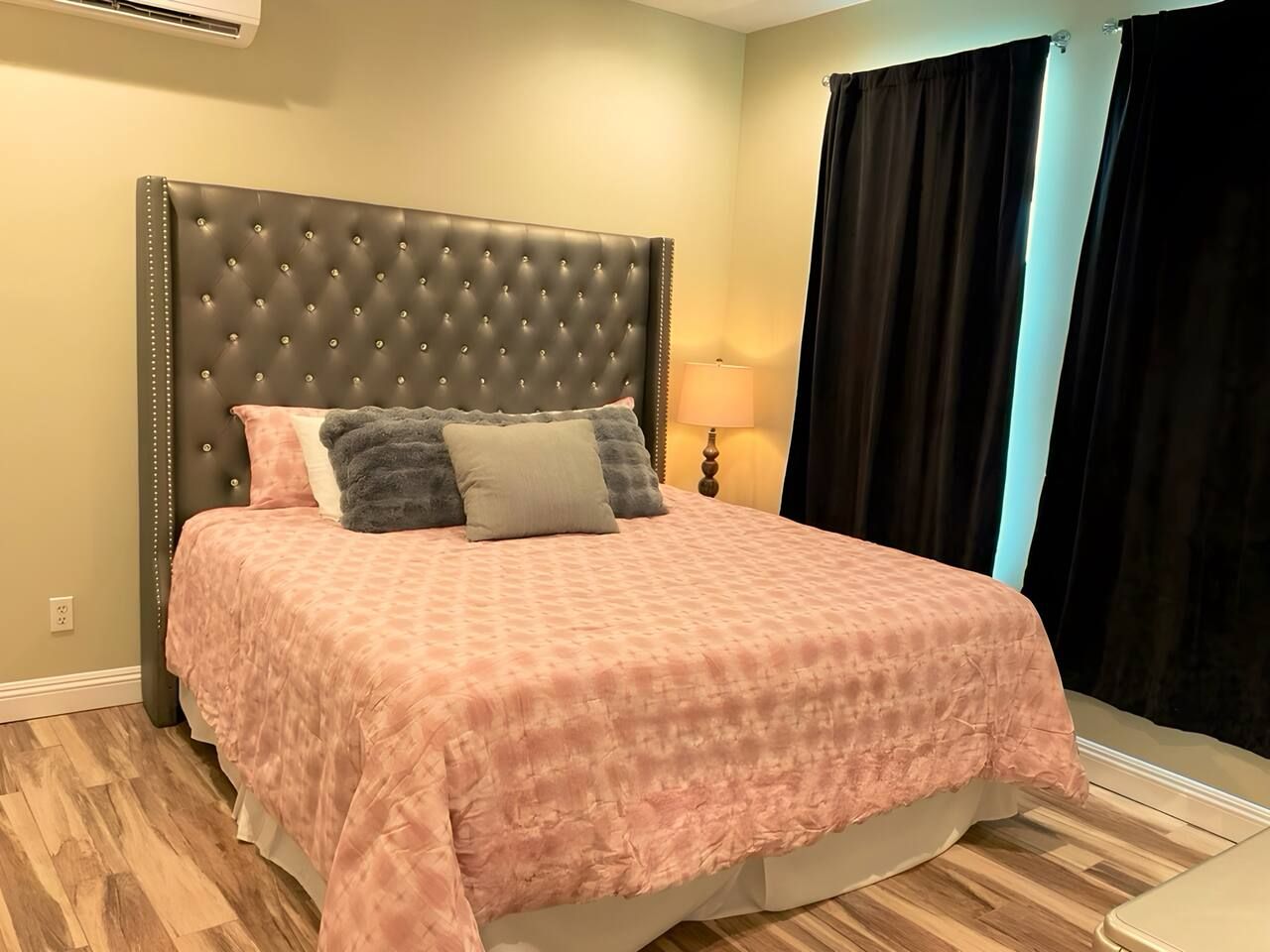 A bed with a tufted headboard, a pink patterned bedspread, and two pillows.