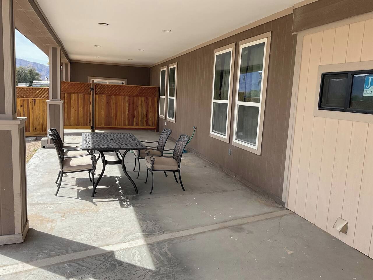 A covered patio area with a table and chairs, wooden fence, and large windows.
