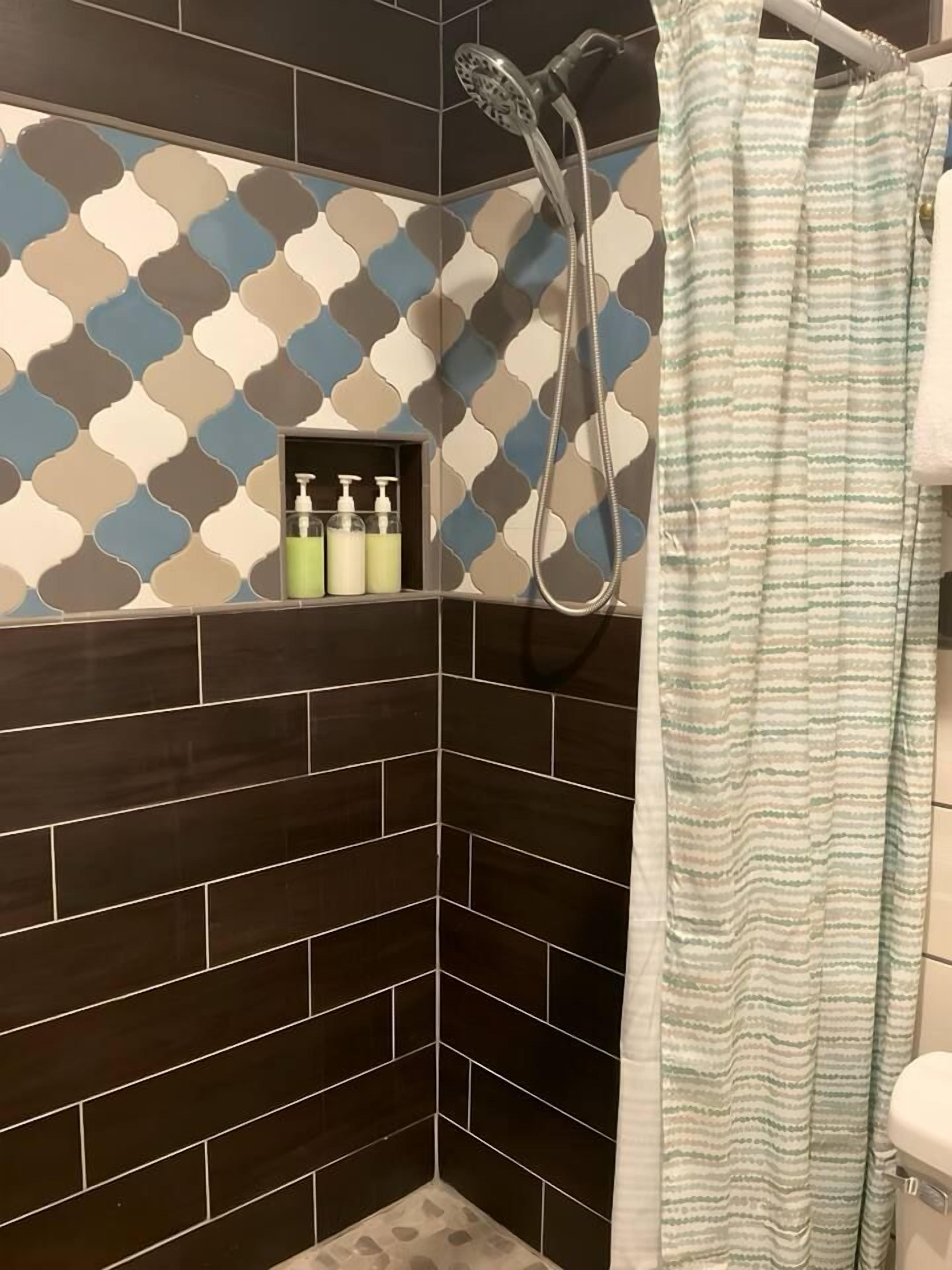 A shower area with a patterned wall, a showerhead, and a striped shower curtain.