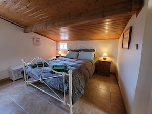 Ein Schlafzimmer mit Metallbettgestell, Holzboden, Nachttisch mit Lampe und Fenster mit Vorhängen.