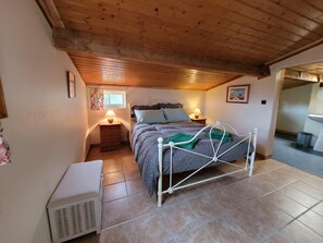 A bedroom with a bed, bedside lamps, a window, a radiator, and a bathroom visible through an open door. - Gite With Garden and Shared Pool (Saint-Saud-Lacoussiere)