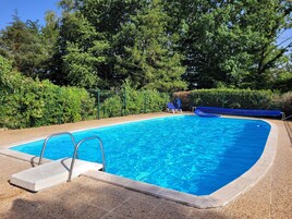 Una piscina azul cristalina con cubierta de madera y escalera metálica, rodeada de abundante vegetación.