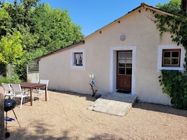 Una casita con camino de grava, una puerta de madera y una ventana con cortinas de encaje.