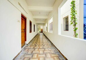 A hallway with patterned flooring, wooden doors, and a plant on the right wall. - Hotel O Pedagantyada Gajuwaka (Visakhapatnam)