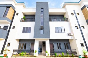 A multi-story building with a central entrance, balconies, and a flat roof. - 3 BEDROOM APARTMENT IN LIFECAMP GWARINPA ABUJA (abuja)