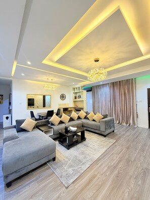 A modern living room with a sectional sofa, a coffee table, and a chandelier. - 3 BEDROOM APARTMENT IN LIFECAMP GWARINPA ABUJA (abuja)