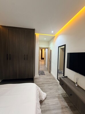 A bedroom with a large bed, wardrobe, and a TV on the wall. - 3 BEDROOM APARTMENT IN LIFECAMP GWARINPA ABUJA (abuja)