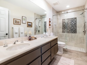 A modern bathroom with a large mirror, dual sinks, a glass shower enclosure, and a tiled shower wall. - Modern Poolside Condo, 2 BR + Flex Space with Bed (Palm Desert)