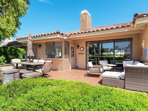 A covered patio with outdoor furniture, a grill, and a large window. - Modern Poolside Condo, 2 BR + Flex Space with Bed (Palm Desert)