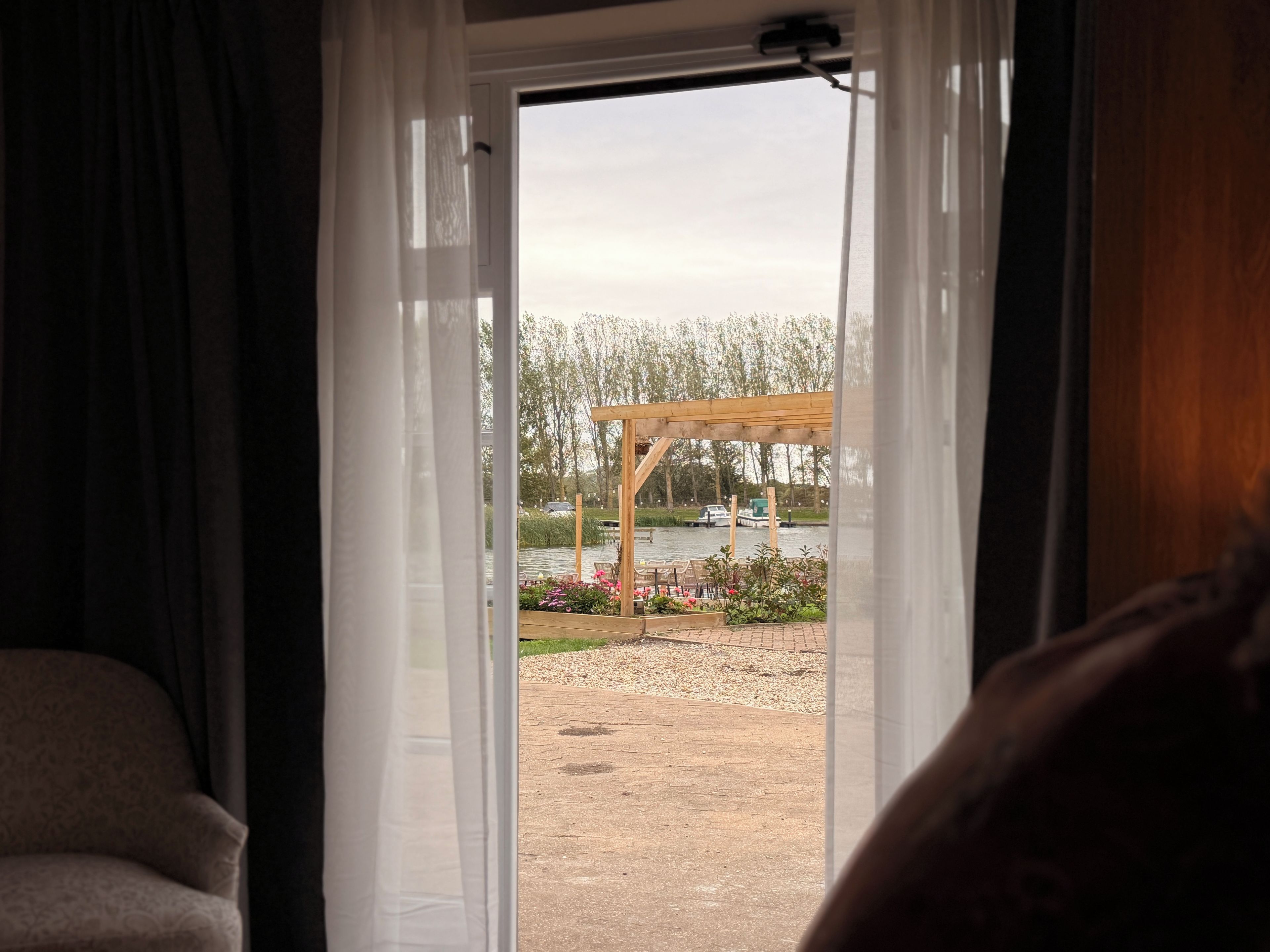 A room with a view of a garden and a wooden pergola outside.