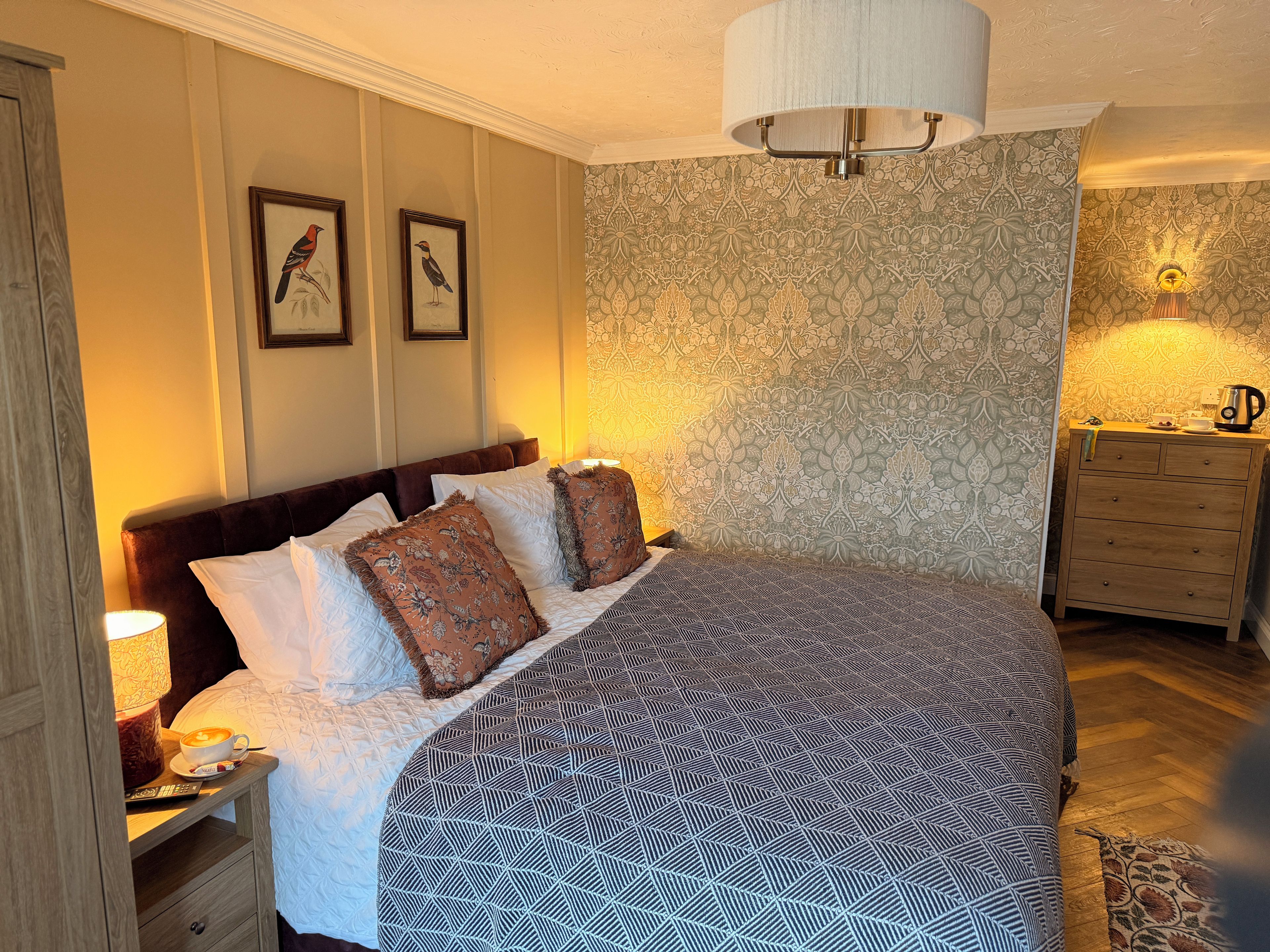 Un dormitorio elegante con una cama grande, una mesita de noche con lámpara, un aparador y una lámpara de pared.