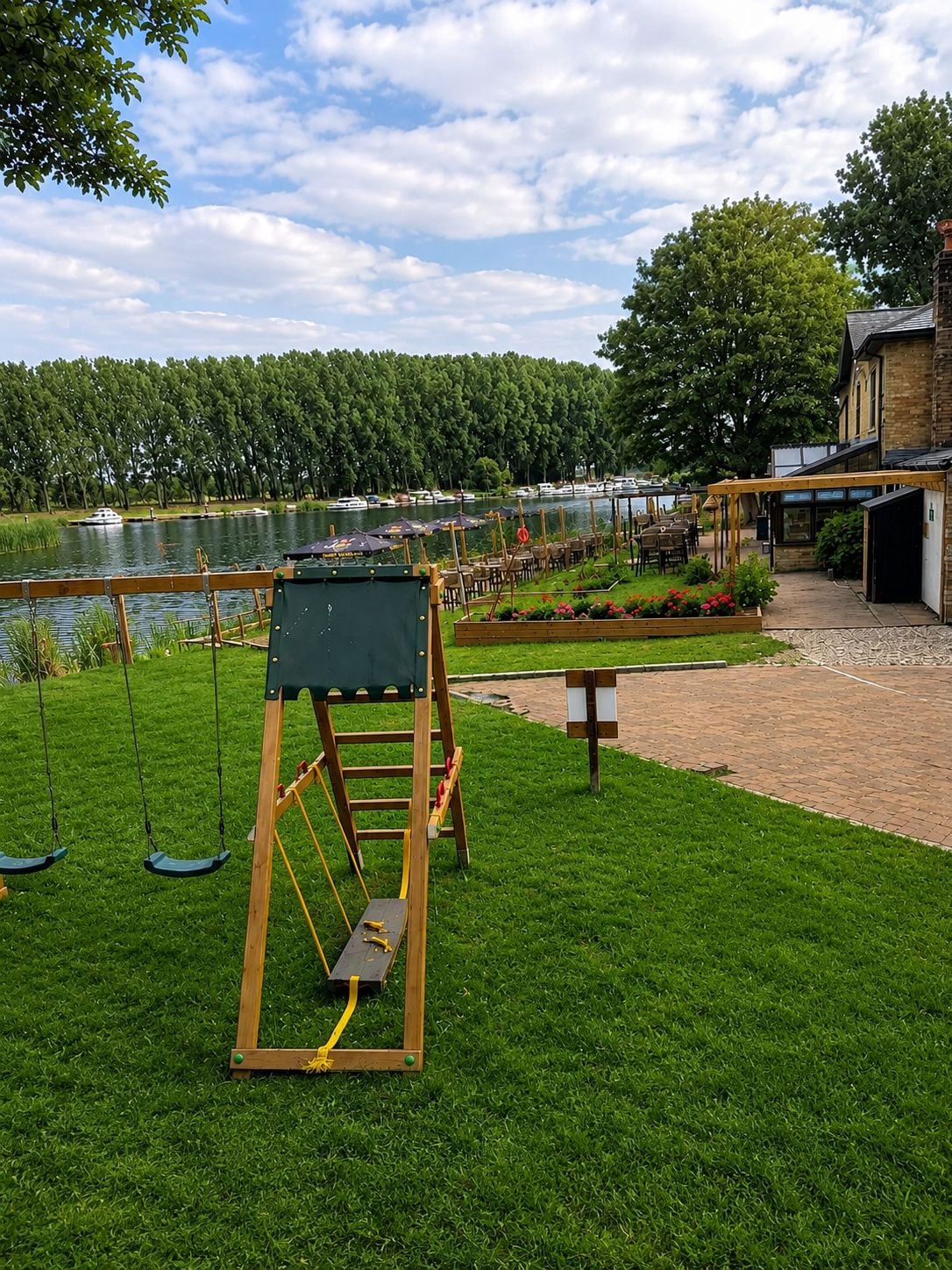 A grassy outdoor area with a swing set, a brick pathway, and a view of a lake with boats.