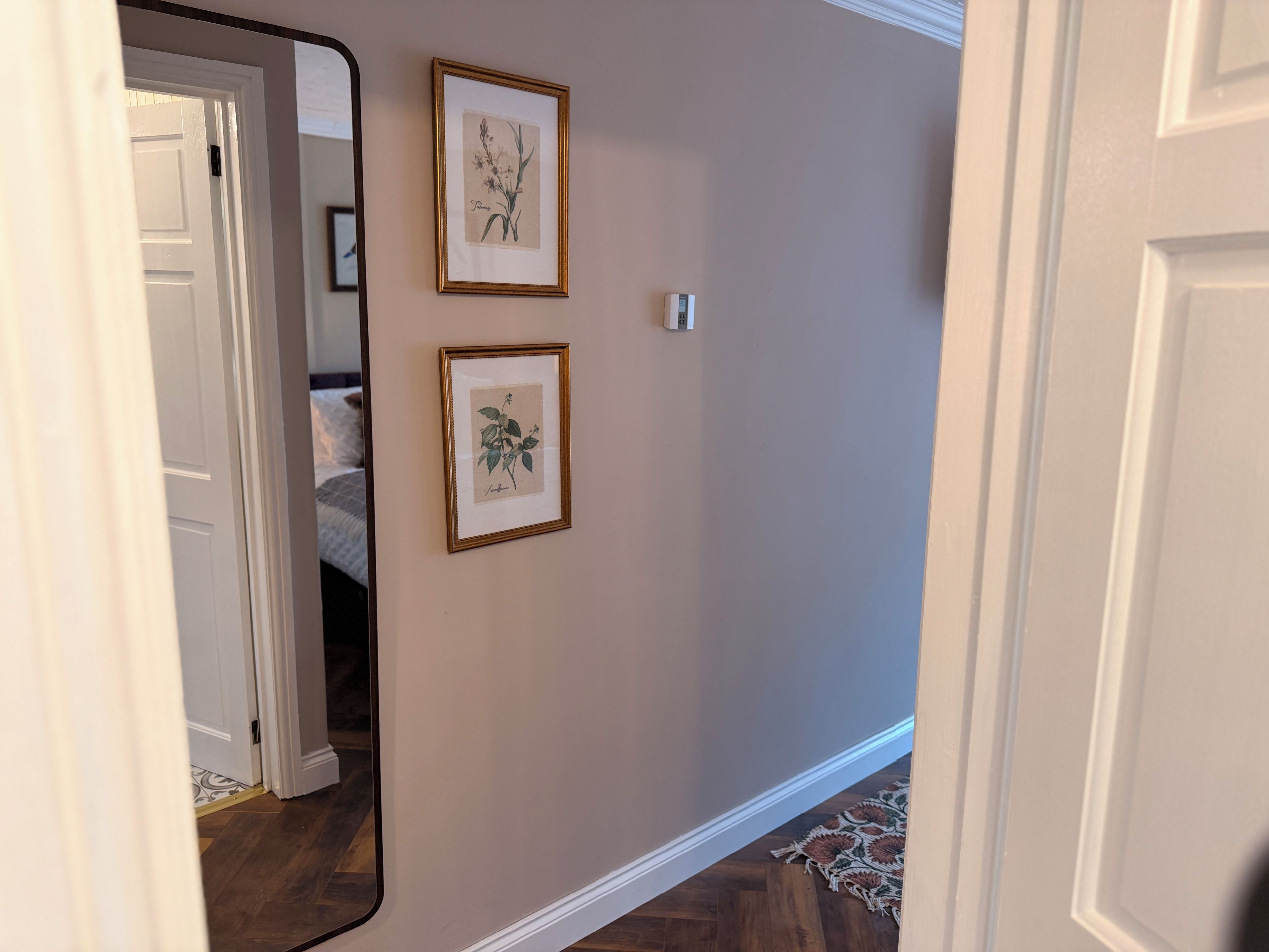 Un pasillo con una puerta que da a un dormitorio, un cuadro botánico enmarcado en la pared y una alfombra estampada en el suelo.