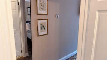 Un pasillo con una puerta que da a un dormitorio, un cuadro botánico enmarcado en la pared y una alfombra estampada en el suelo.