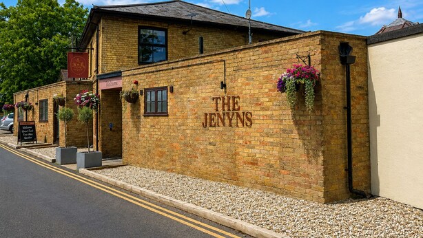 A brick building with 'THE JENYNS' signage, a welcoming signboard, and flower baskets on the wall. - the Jenyns  (Denver)