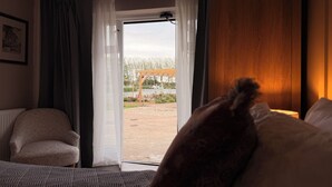 A hotel room with a bed, a chair, a wooden wardrobe, and a view of the outdoors through a glass door. - the Jenyns  (Denver)
