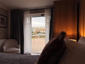 Hotellihuone, jossa on sänky, tuoli, puinen vaatekaappi ja lasiovesta avautuva näkymä ulos.