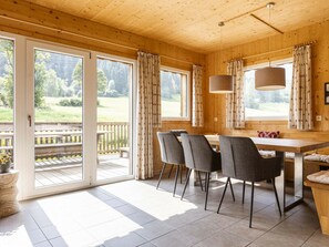 A wooden interior with a dining table, chairs, and a view of a deck. - One-bedroom Cabin (Sankt Georgen am Kreischberg)