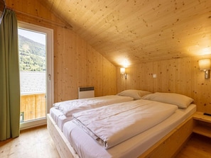 Ein Zimmer aus Holz mit einem Bett, einem Fenster und Blick auf eine gebirgige Landschaft.