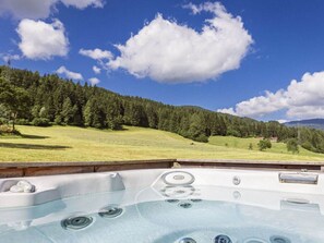Un jacuzzi con vistas despejadas a una ladera boscosa y una casa a lo lejos.