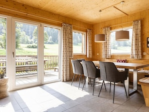 Un interior de madera con una mesa de comedor, sillas y vistas a una terraza.