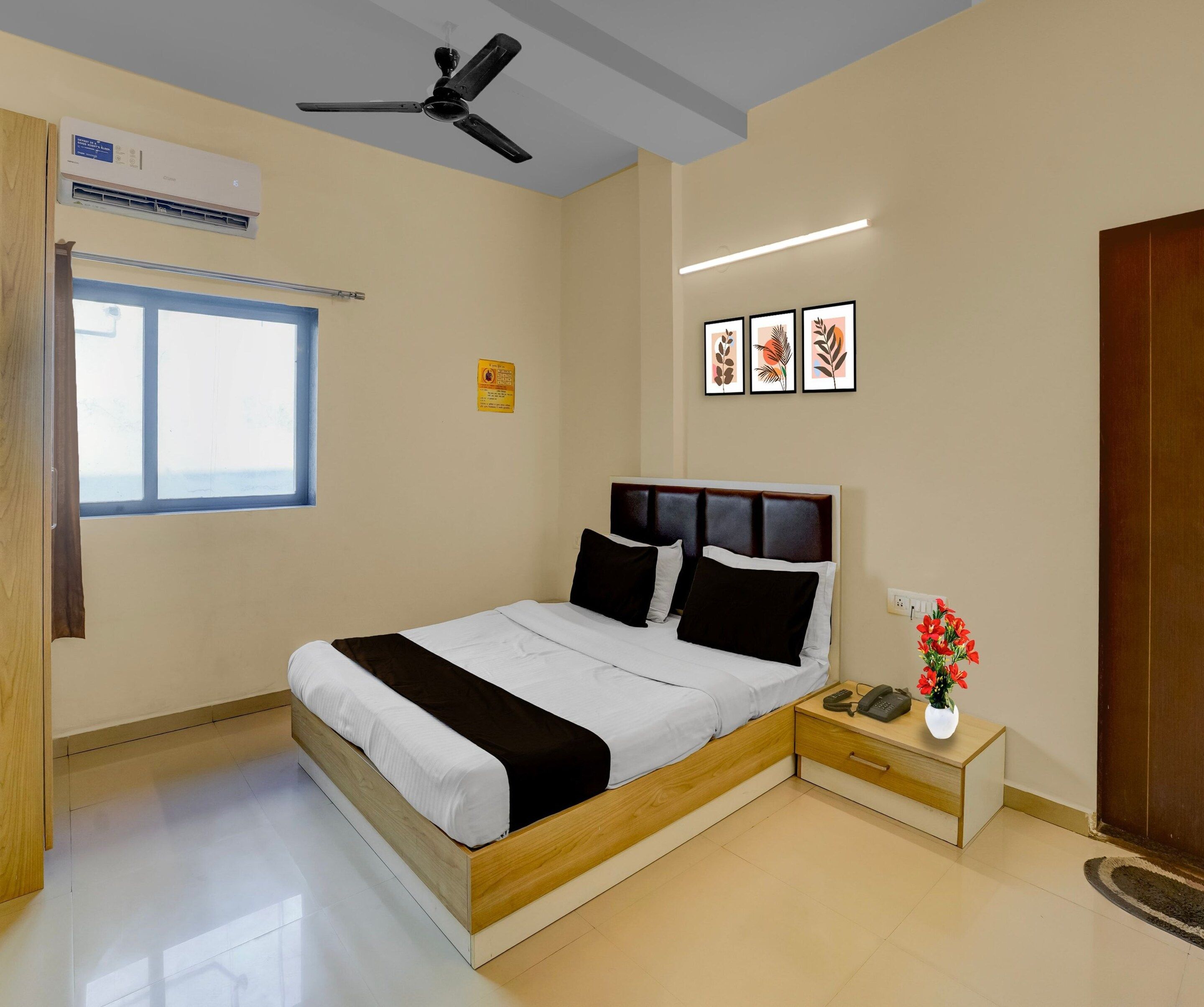 A hotel room with a bed, bedside table, a phone, a vase with flowers, and a ceiling fan.