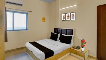 A hotel room with a bed, bedside table, a phone, a vase with flowers, and a ceiling fan.