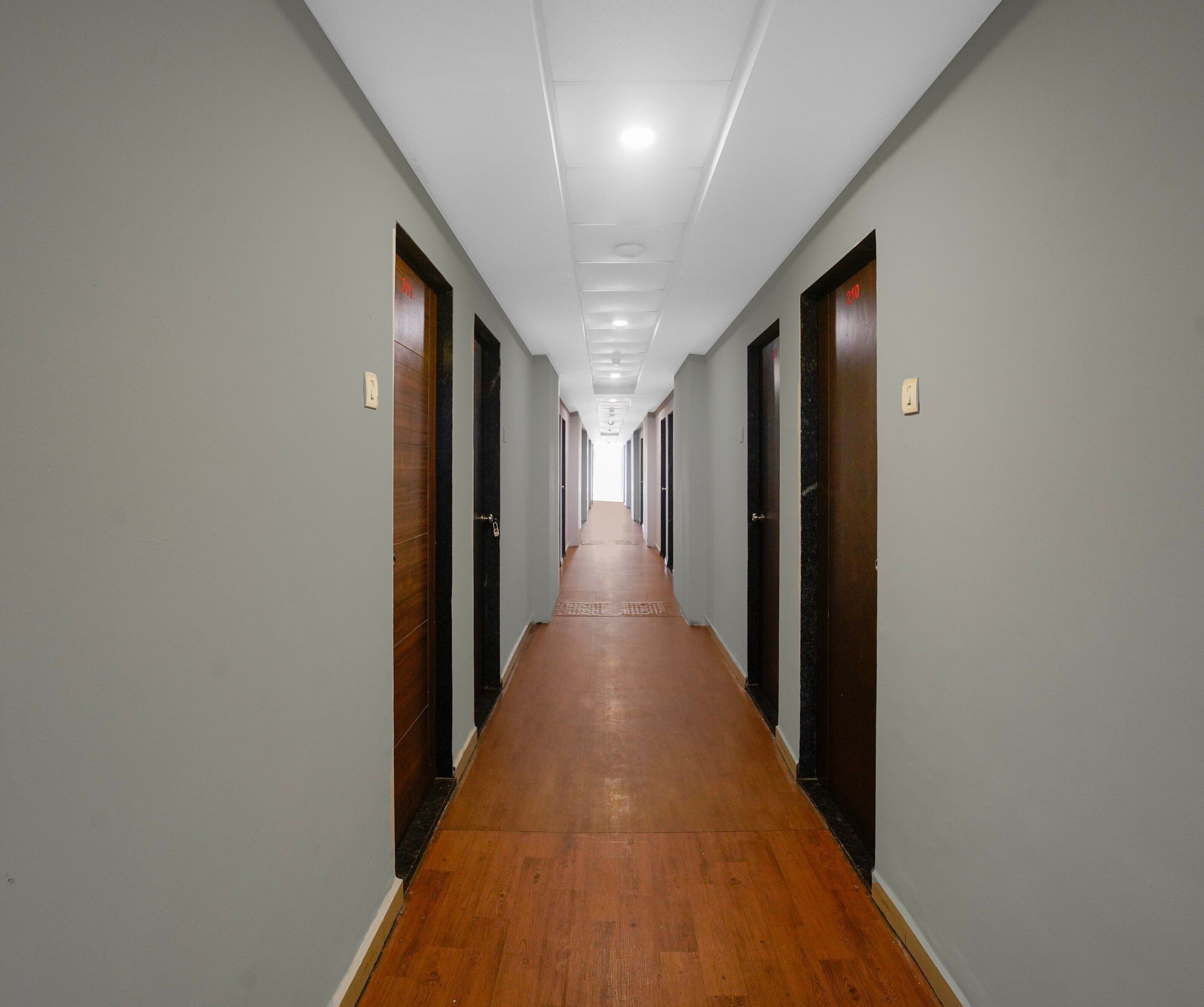 Un pasillo largo y estrecho con suelo de madera y puertas a ambos lados, que conduce a un espacio abierto al final.