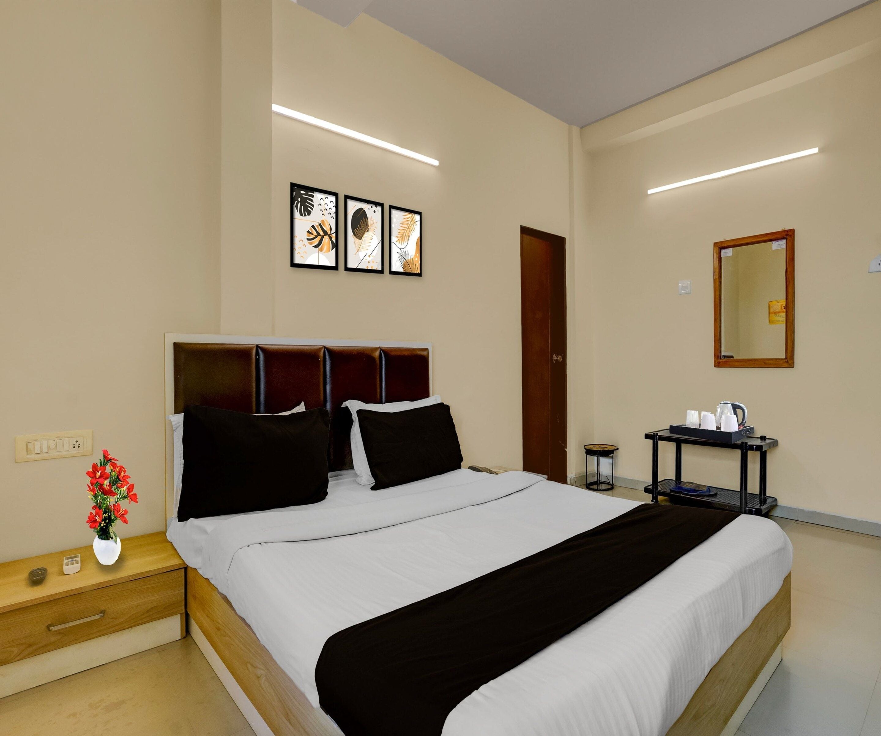 Una camera d'albergo con un letto, un comodino, un piccolo tavolo con un vaso di fiori, uno specchio e opere d'arte appese al muro.
