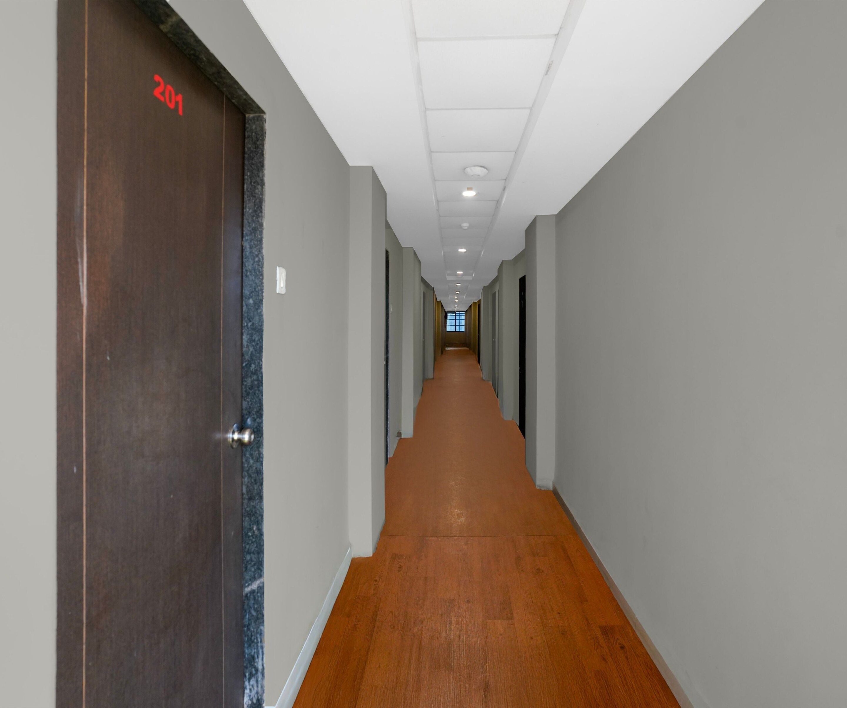 Un largo y estrecho pasillo con piso de madera y paredes grises, que conduce a una puerta con el número 201.