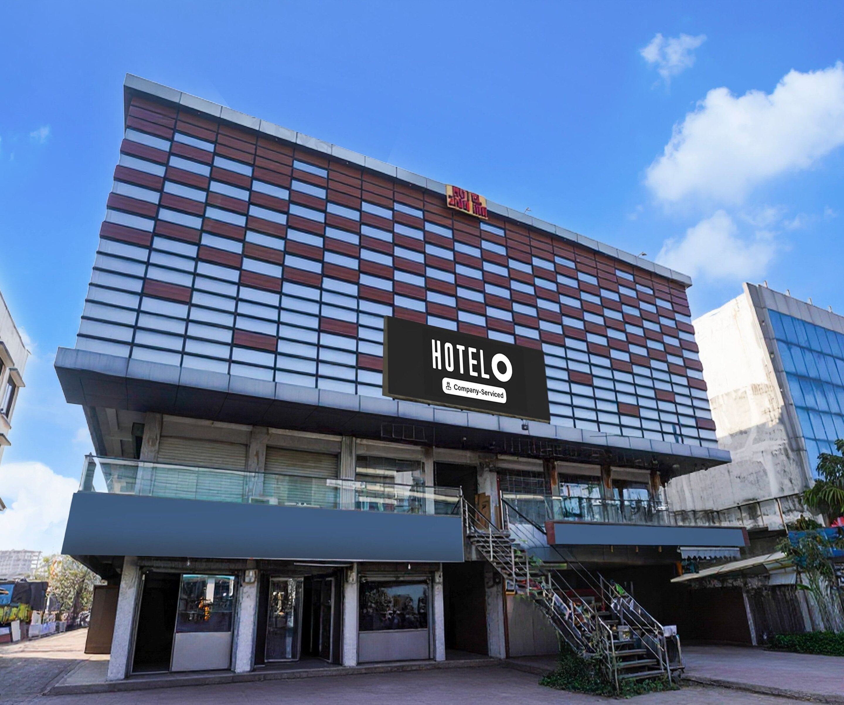 A hotel with a modern facade, a prominent sign indicating it is a company-serviced hotel, and a staircase leading to the entrance.