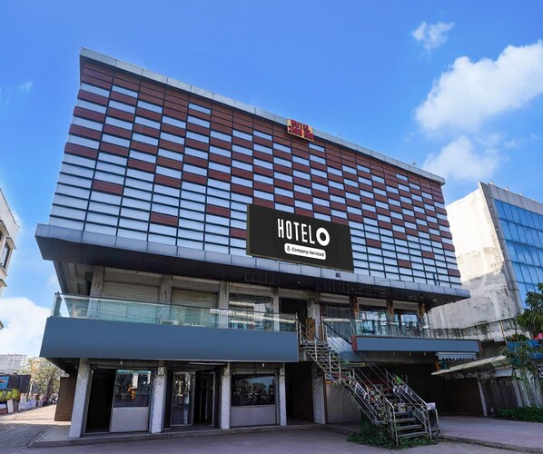 A hotel with a modern facade, a prominent sign indicating it is a company-serviced hotel, and a staircase leading to the entrance.