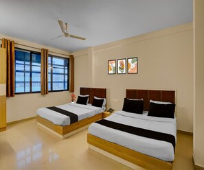 Habitación de hotel con dos camas, un ventilador de techo, una ventana con cortinas y tres obras de arte en la pared.