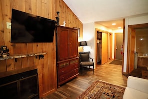 A living room with a fireplace, a television mounted on the wall, a wooden cabinet, a chair, and a rug.