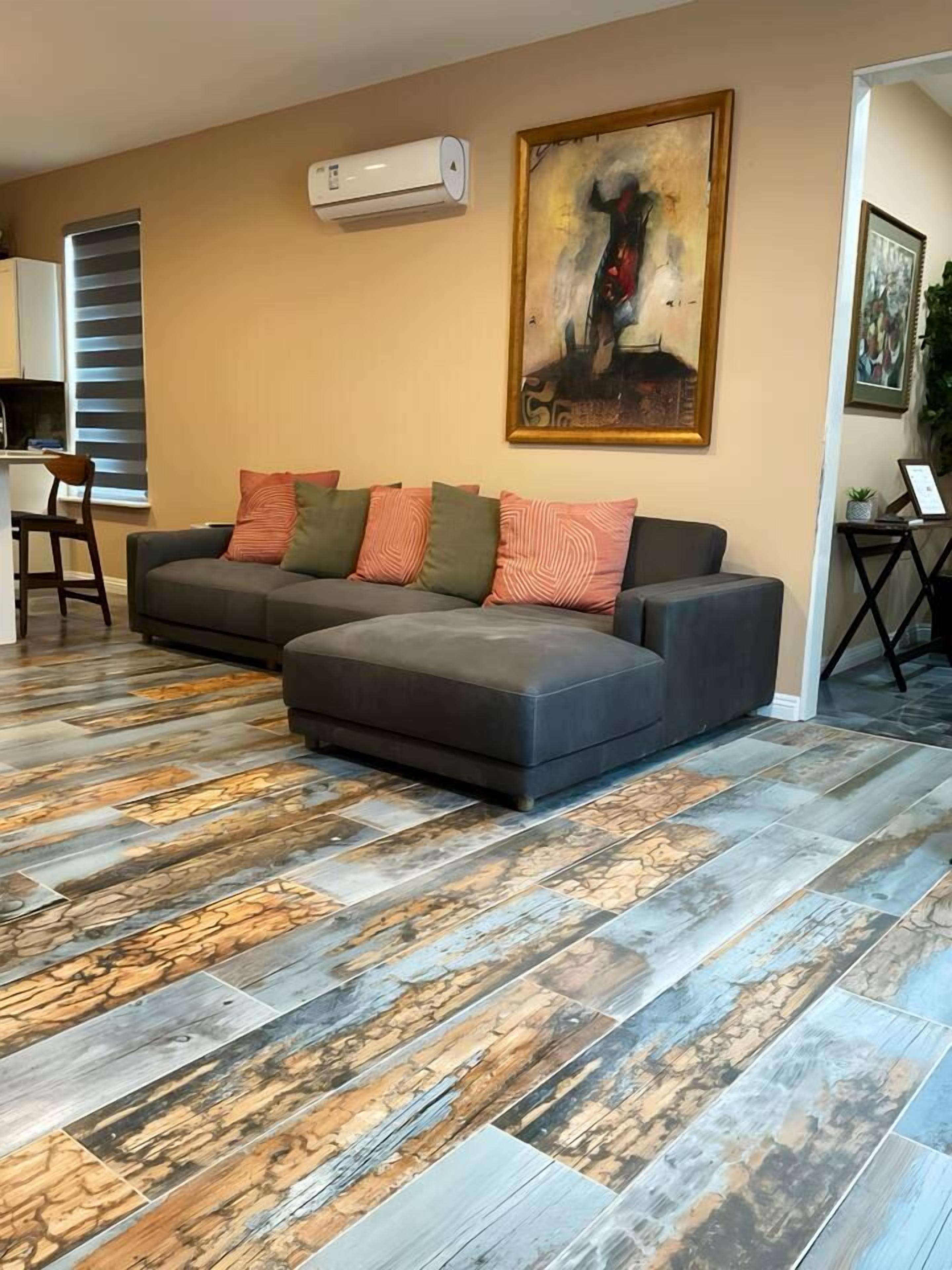 Un salon avec un canapé d’angle, un tableau et un sol à motifs.