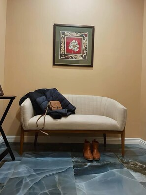 A beige sofa with a brown leather bag and a pair of brown shoes on a blue patterned rug. A framed picture hangs on the wall above the sofa.