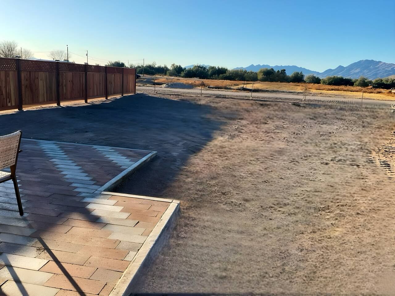 A paved patio area with a wooden fence, a bench, and a view of a dry landscape with mountains in the distance.