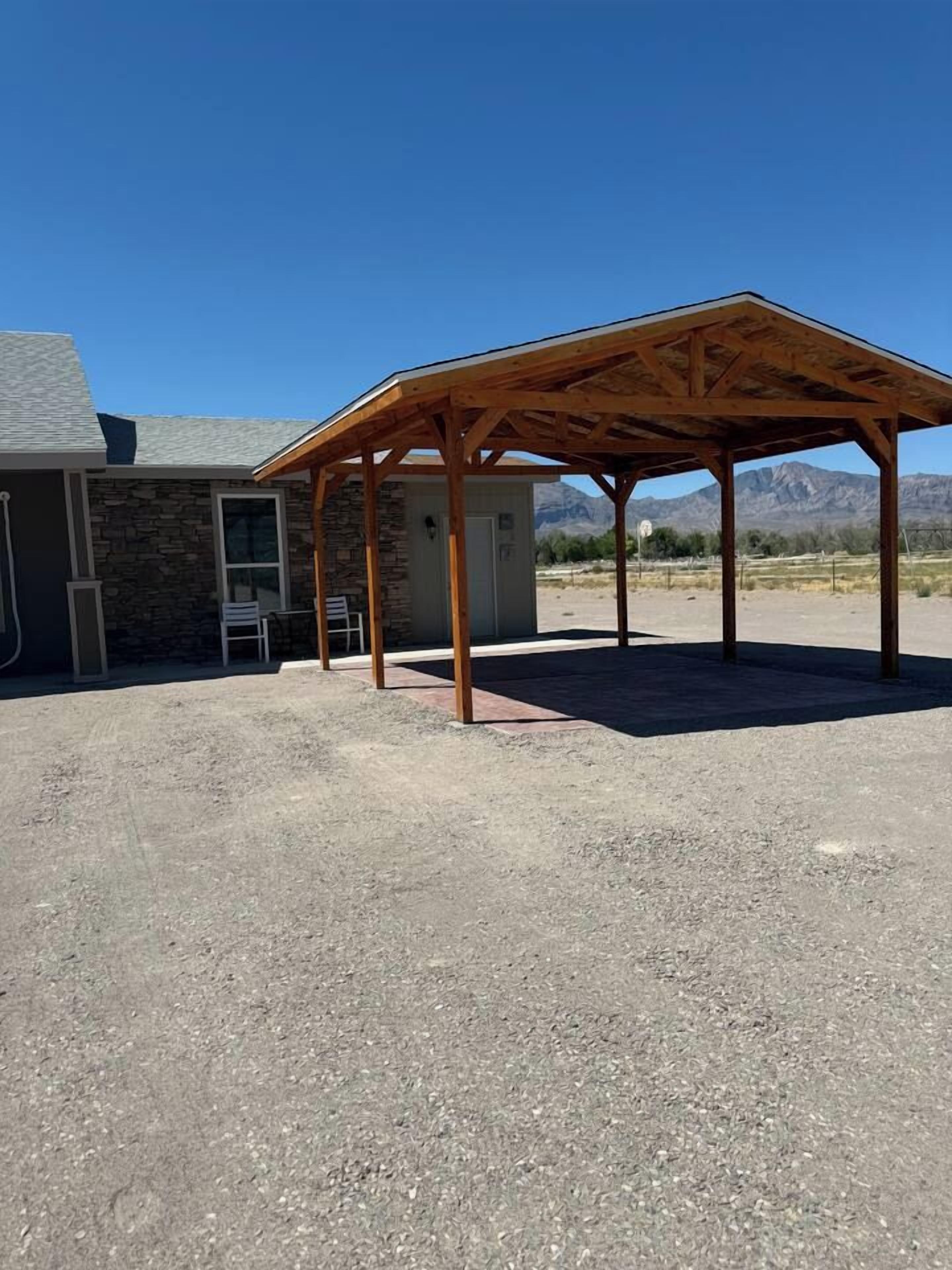 A covered outdoor area with a gravel ground, a stone building, and a mountain backdrop.