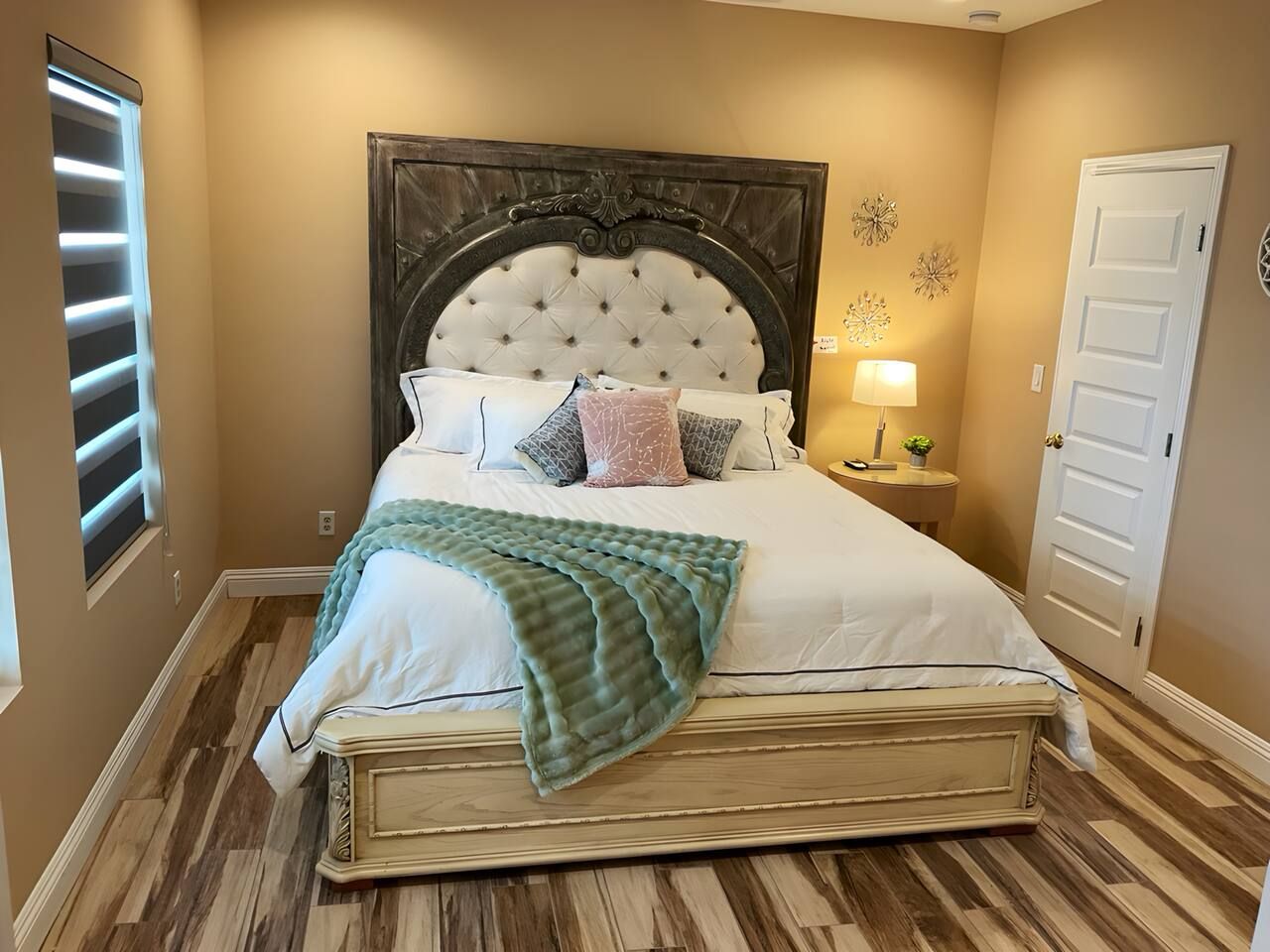 A bedroom with a large bed, a nightstand, a lamp, and a door.