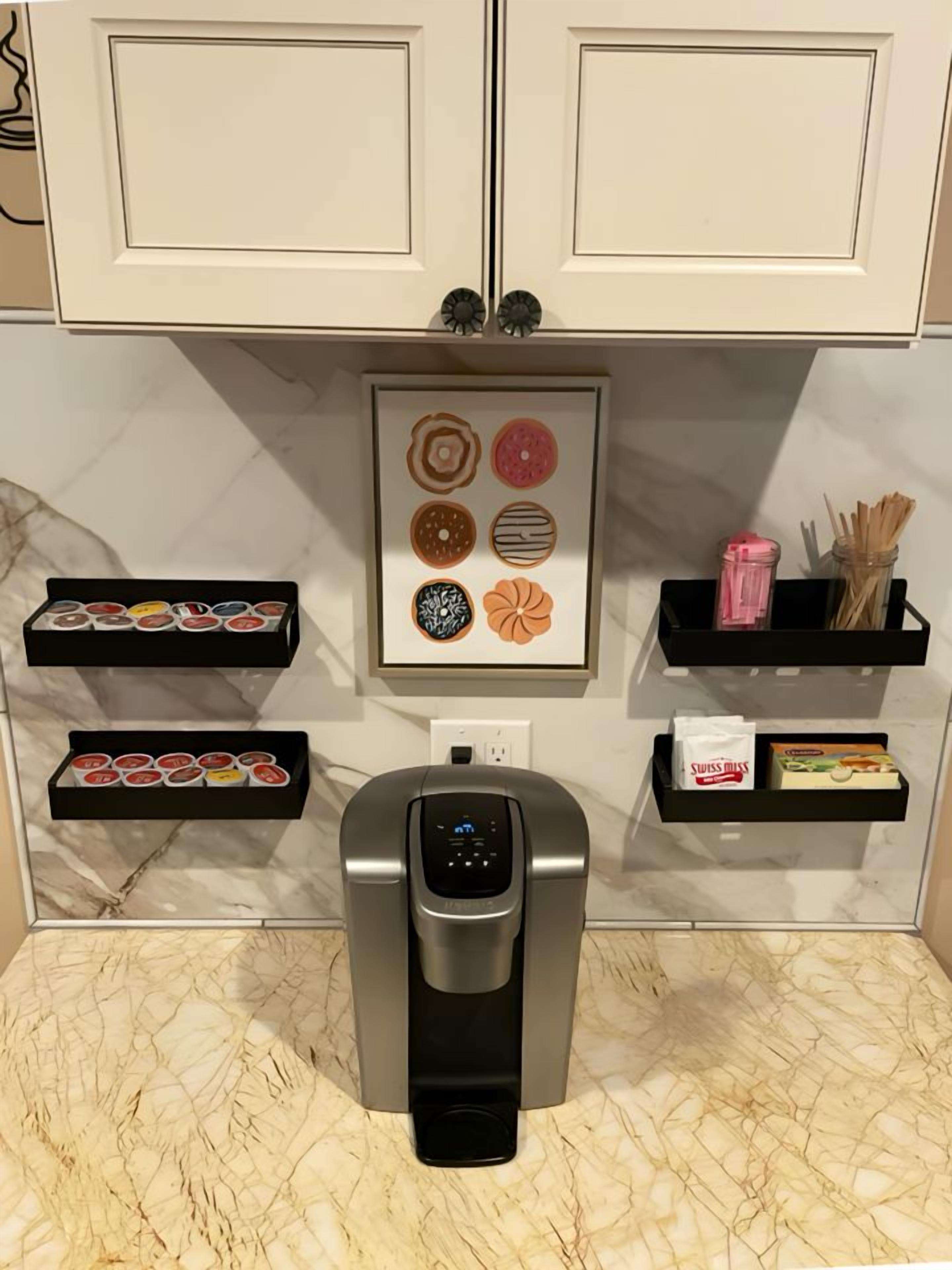 A kitchen with a built-in espresso machine, two black shelves with food items, and a framed picture of donuts.