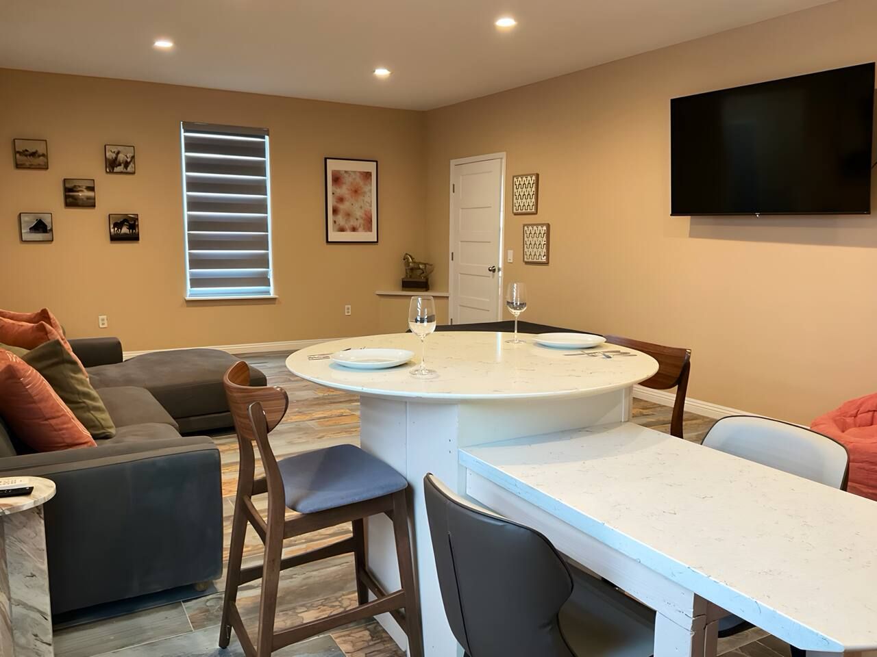 A living room with a round dining table, a sofa, and a television mounted on the wall.