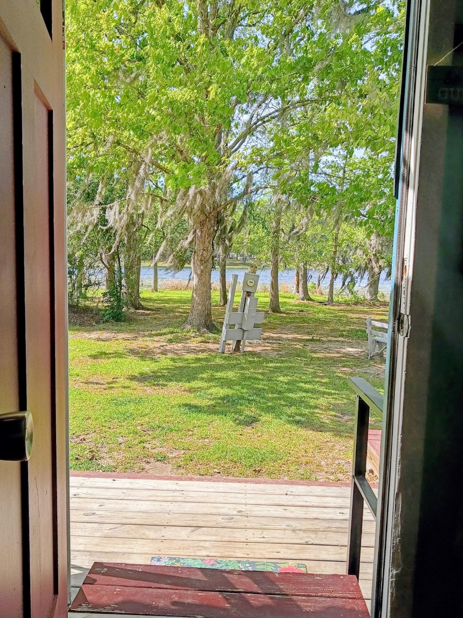 A wooden deck leading to a grassy area with trees and a body of water in the background.