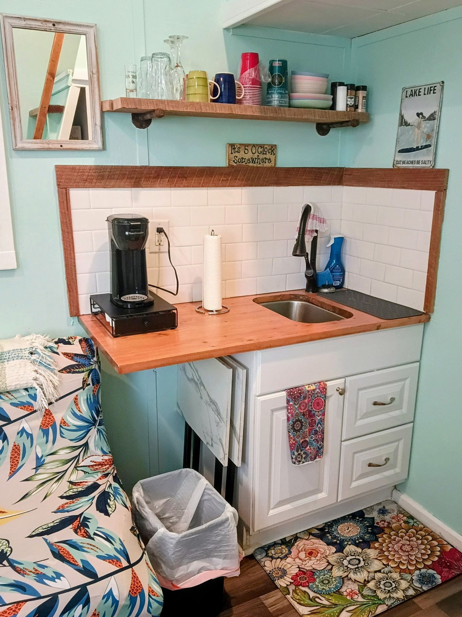 A compact kitchen with a coffee maker, a sink, and a small trash bin.
