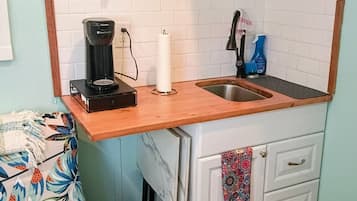 A compact kitchen with a coffee maker, a sink, and a small trash bin.
