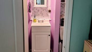 A narrow bathroom with a white sink, a mirror, and a door leading to another room.