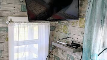 A room with a bed, a television mounted on the wall, a window with a curtain, and a wall with a wooden panel design.