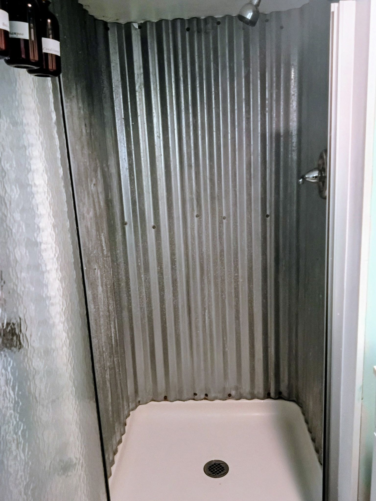 A small, enclosed shower area with a corrugated metal wall and a white floor.