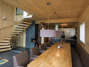 A modern interior with a wooden staircase, a central dining table with chairs, a kitchen area, and a fireplace. - Cabin With 1 Bedroom (Sankt Georgen am Kreischberg)