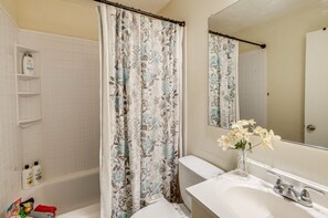 Een badkamer met een bad, een douchegordijn met bloemendesign, een wastafel met spiegel en toiletartikelen aan de muur.