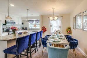 Una cocina moderna con armarios blancos, una isla central y sillas de terciopelo azul.